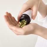 Hands,Pouring,Green,Herbal,Capsules,From,Bottle,Into,An,Open