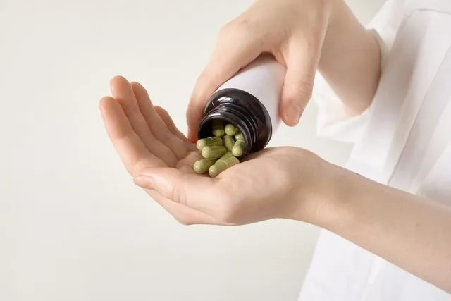 Hands,Pouring,Green,Herbal,Capsules,From,Bottle,Into,An,Open