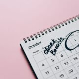 Calendar de perete cu zile bifate cu marker, lângă o cană și o carte