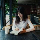 Caiet deschis cu un citat scris de mână, un stilou și o cană de cafea pe o masă de lemn